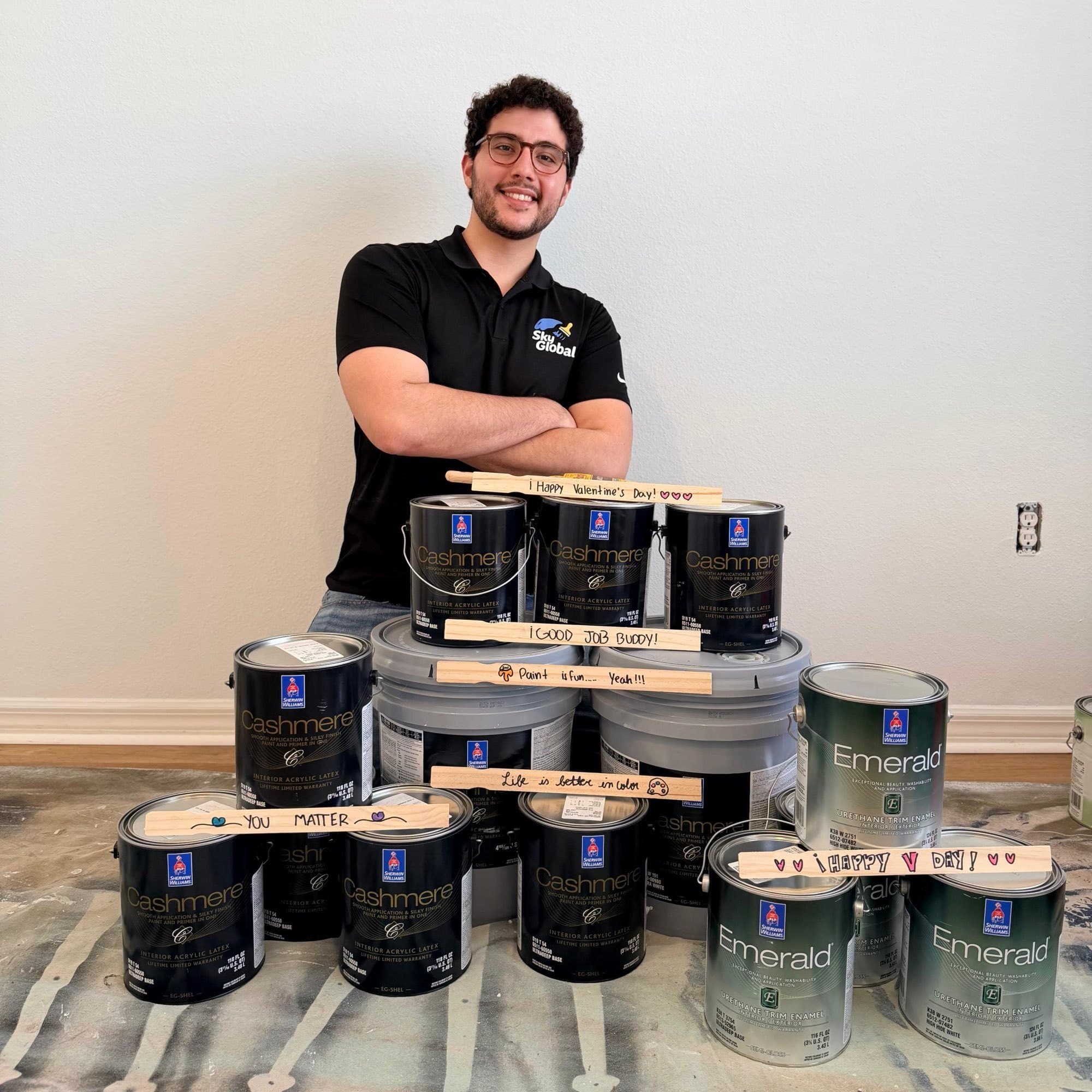 Iker in a SkyGlobal polo behind a stack of Sherwin-Williams Cashmere and Emerald cans, with handwritten stir sticks left by the crew.