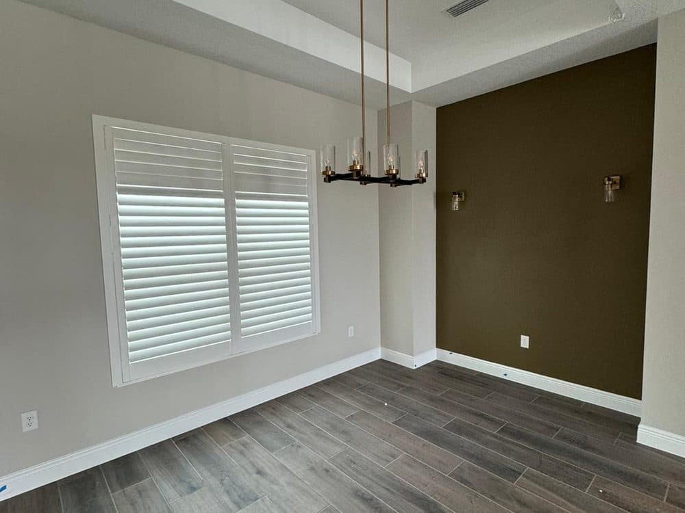 Interior repaint — dining room with an olive-green accent wall, white trim, and plantation shutters.