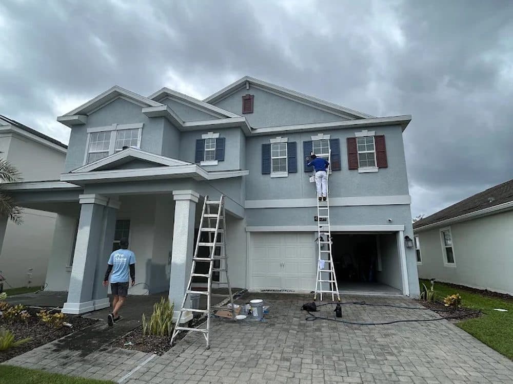 Exterior repaint in progress — two-story home with the crew on ladders cutting in the upper floor.